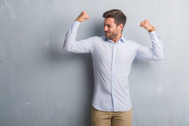 Şık gömlek gösteren kol kasları gururlu gülümseyen giyen gri grunge duvarın üzerinden yakışıklı genç iş adamı. Fitness kavramı.