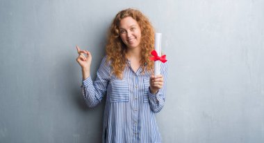 Genç redhead iş kadını diploması çok mutlu el ve parmak ile tarafına işaret tutan gri grunge duvarın üzerinden