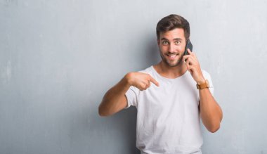 Yakışıklı delikanlı kendisine sürpriz yüz işaret parmağı ile telefonda konuşan gri grunge duvarın üzerinden