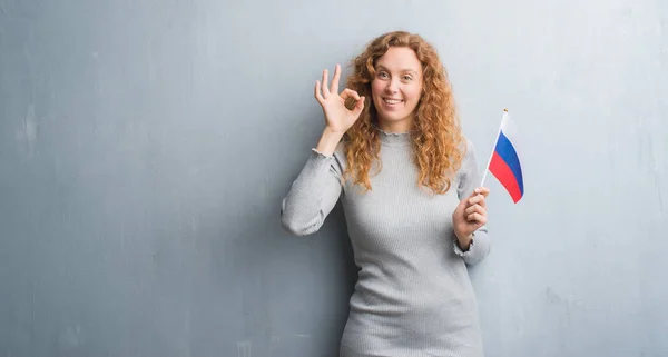 Joven Pelirroja Sobre Gris Grunge Pared Sosteniendo Bandera Rusia Haciendo —  Fotos de Stock