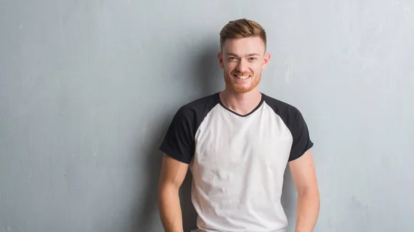 Young redhead man over grey grunge wall with a happy and cool smile on face. Lucky person.