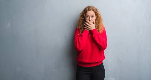 年轻的红发女人在灰色的难看的垃圾墙穿红色毛衣震惊地捂着嘴与手错误 秘密概念 — 图库照片