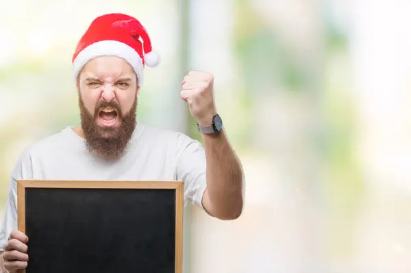 年轻的高加索嬉皮士男子戴着圣诞帽 在孤立的背景惹恼和沮丧的喊声与愤怒 疯狂和大喊大叫 举起的手 愤怒的概念 — 图库照片