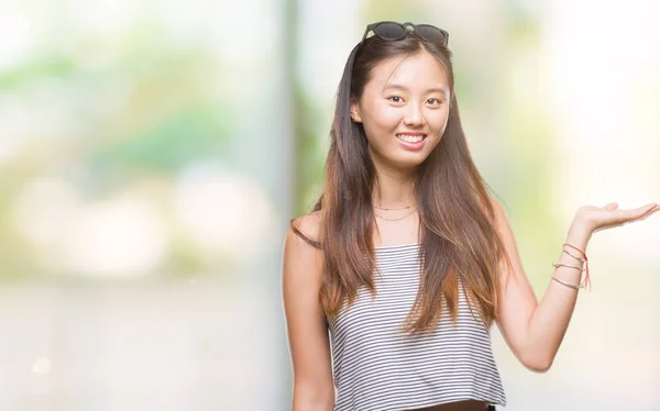 年轻的亚洲妇女戴着太阳镜在孤立的背景下微笑欢快地呈现和指向与手掌看着相机 — 图库照片