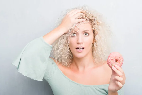 Joven Rubia Sobre Fondo Gris Grunge Comiendo Rosquilla Estresada Con —  Fotos de Stock