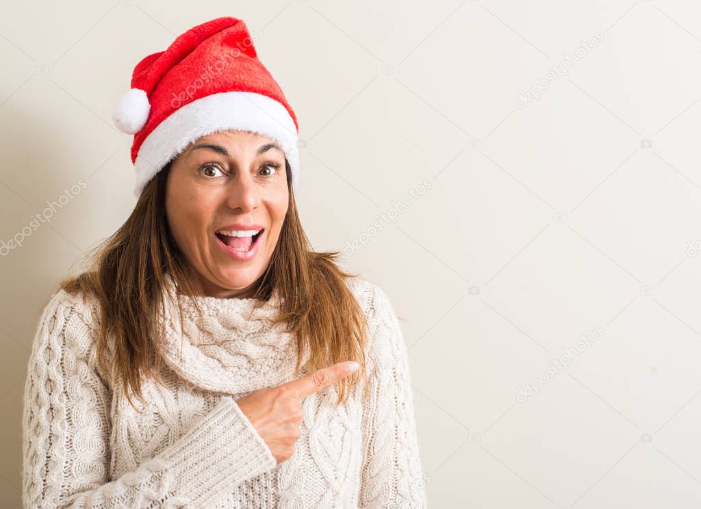 Middle age woman wearing christmas santa claus hat very happy pointing with hand and finger