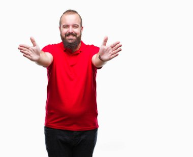 Sarılmak için kollarını açarak gülümseyerek kameraya bakarak izole arka plan üzerinde kırmızı gömlek giymiş genç beyaz hipster adam. Neşeli ifade kucaklayan mutluluk.