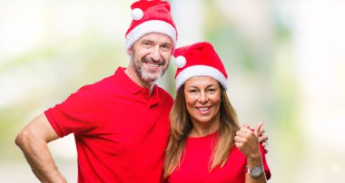 Orta yaş İspanyol çift arıyorum ve başparmak yanında yukarıyı mutlu yüz ile gülümseyen izole arka plan üzerinde Noel şapka.