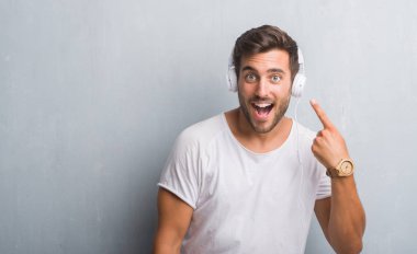 El ve parmak ile işaret çok mutlu müzik dinlerken kulaklık giyen gri grunge duvarın üzerinden yakışıklı genç