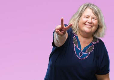 Kıdemli artı boyutu arka plan zafer işareti yapıyor parmak gösterilen kameraya gülümseyen seyir beyaz kadın izole. İki numaralı.