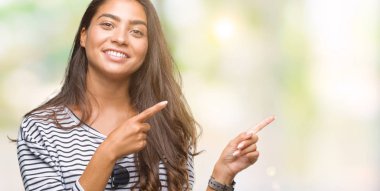 Genç güzel Arap kadın gülümseyerek ve iki elleri ve parmakları ile tarafına işaret kamera bakarak izole arka plan üzerinde güneş gözlüğü takıyor.