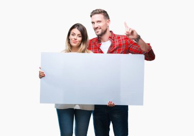 Boş bir arada tutan genç çift izole arka bir fikirle sürpriz üzerinde banner veya gülen yüz, bir numara ile işaret parmağı soru