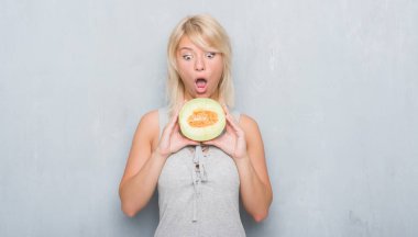 Kavun karpuz bir sürpriz yüz, korkuyor ve heyecanlı korku ifadesi ile şok korkmuş yeme grunge gri duvar yetişkin beyaz kadın