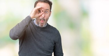 Sürpriz yüz, göz parmaklarının arasından seyir ile ok jest yapıyor izole arka plan üzerinde bir kazak giyen yakışıklı orta yaş üst düzey adam şok. İmansız ifade.