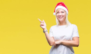 Kameraya bakarak yan el ve parmak ile işaret yüzünde kocaman bir gülümseme ile izole arka plan üzerinde Noel şapka giyen genç güzel sarışın kadın.