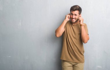 Yüksek sesle müzik gürültü rahatsız ifade parmaklarıyla kulaklarıyla kapsayan gri grunge duvarın üzerinden yakışıklı genç adam. Sağır kavramı.