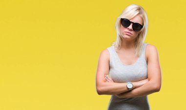 Genç güzel sarışın kadın izole arka plan şüpheci ve sinir, onaylamayan ifade yüz çapraz kolları üzerinde güneş gözlüğü takıyor. Negatif kişi.