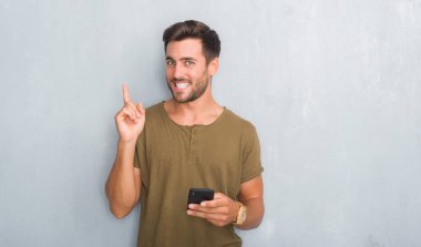 Yakışıklı genç gri grunge üzerinde duvar manifatura smartphone el ve parmak ile tarafına işaret çok mutlu kullanarak bir ileti
