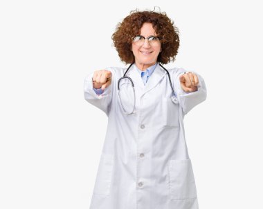 Orta ager kıdemli doktor kadın izole arka plan yüzünden seni ve kameraya gülümseyen pozitif ve neşeli parmaklarıyla işaret