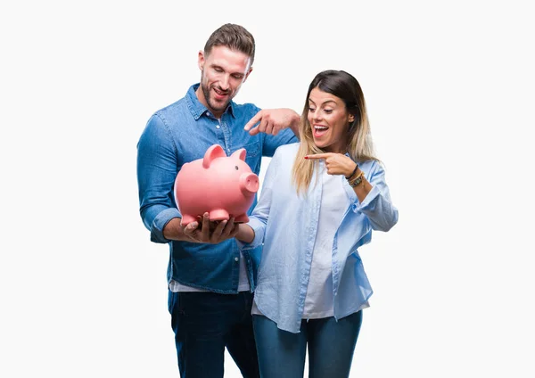 Young couple in love holding piggy bank over isolated background very happy pointing with hand and finger