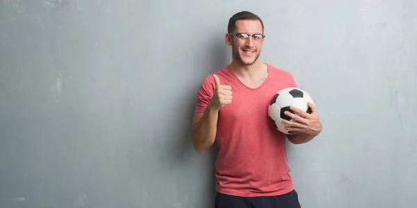 Νεαρός Καυκάσιος Πάνω Από Τοίχο Γκρι Grunge Κρατώντας Ποδόσφαιρο Ποδόσφαιρο — Φωτογραφία Αρχείου
