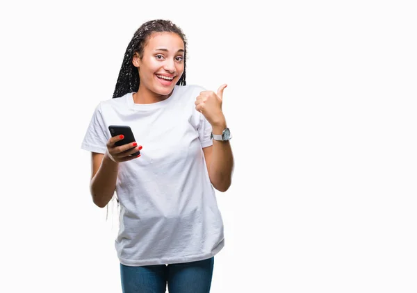 年轻的编织头发非洲裔美国女孩显示使用智能手机在孤立的背景指向和显示与快乐的脸微笑的一侧与拇指 — 图库照片