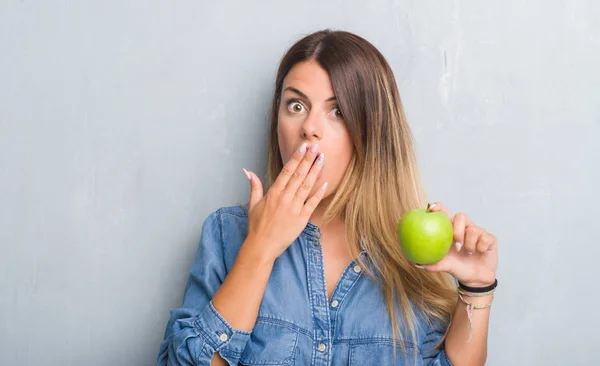 年轻的成年妇女在灰色的垃圾墙吃新鲜的绿色苹果盖口与手震惊与羞愧的错误 表达恐惧 害怕在沉默中 秘密概念 — 图库照片