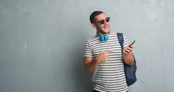 Молодий Білий Студент Над Сірою Гранжевою Стіною Навушниках Використовуючи Смартфон — стокове фото