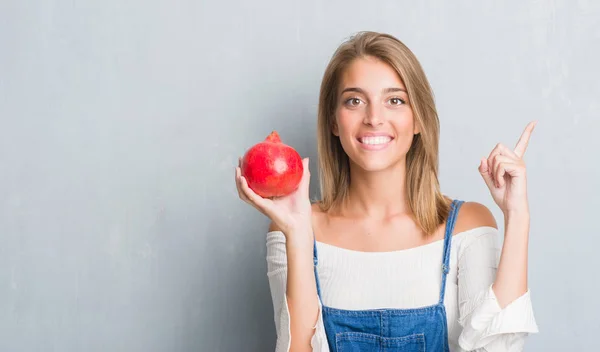 Schöne Junge Frau Über Grunge Graue Wand Hält Granatapfel Überrascht — Stockfoto