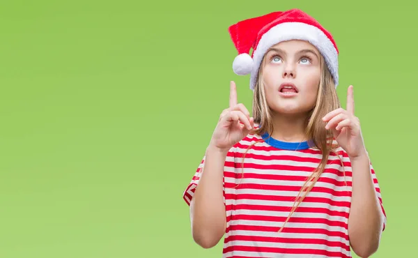 年轻美丽的女孩戴着圣诞节帽子在孤立的背景惊讶和惊讶抬起手指和举起的胳膊 — 图库照片