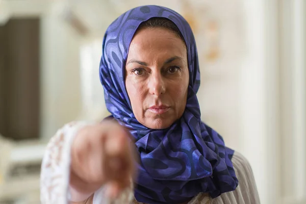 Middle age brunette arabian woman wearing colorful hijab pointing with finger to the camera and to you, hand sign, positive and confident gesture from the front