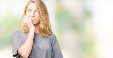 Stresli ve gergin elle çivi ısırma ağzına bakarak izole arka plan üzerinde büyük boy rahat t-shirt giyen güzel ve genç birbayan. Anksiyete sorunu.