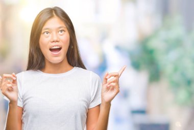 Genç Asyalı kadın izole arka plan üzerinden hayran ve yukarıya bakıp parmakları ile işaret şaşırttı ve silah kaldırdı.