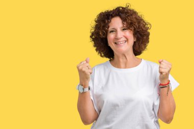 Üzerinde izole arka plan kutluyor t-shirt şaşırttı ve silah ile başarı için hayran beyaz giyen güzel orta ager üst düzey kadın kaldırdı ve gözleri açık. Kazanan kavramı.