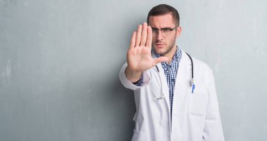 Doktor ile üniforma giyen gri grunge duvarın üzerinden beyaz delikanlı dur işareti ile ciddi ve kendine güvenen ifade, savunma hareketi yaparken el açmak