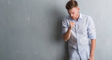 Genç redhead iş adamı hasta ve soğuk veya bronşit için semptom olarak öksürük duygu gri grunge duvarın üzerinden. Sağlık kavramı.
