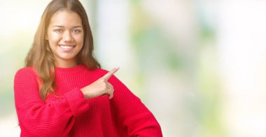 Üzerinde izole kırmızı kış kazak giyen genç güzel esmer kadın yan gösteren reklam, ciddi ve sakin yüz el parmak ile işaret arka plan