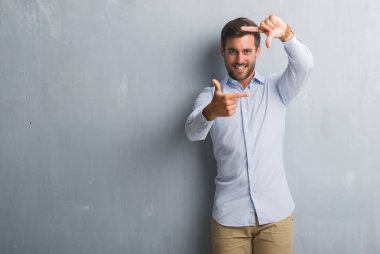 Yakışıklı genç iş adamı gri grunge üzerinde duvar elle yapma çerçeve ve parmakları ile mutlu yüz gülümseyen giyen şık gömlek. Yaratıcılık ve Fotoğrafçılık kavramı.