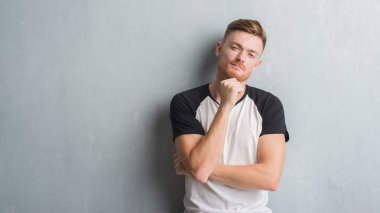 Emin çapraz kollar ve çeneme kaldırdı el ile gülümseme ile kamera seyir gri grunge duvarın üzerinden genç Kızıl saçlı adam. Pozitif düşünce.