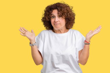 Üzerinde beyaz t-shirt giyen güzel orta ager üst düzey kadın arka plan clueless ve şaşkın bir ifadeyle kollar ve eller kaldırdı izole. Şüphe kavramı.