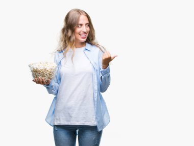 İşaret ve başparmak kadar mutlu yüz gülümseyen tarafı ile gösteren izole arka plan üzerinde patlamış mısır yemek güzel sarışın genç kadın