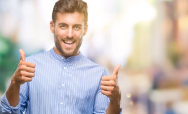 Yakışıklı delikanlı izole arka plan başarı işareti el ile pozitif jest yapıyor üzerinde başparmak gülümseyen ve mutlu. Neşeli bir ifadeyle, kazanan jest kameraya bakıyor.