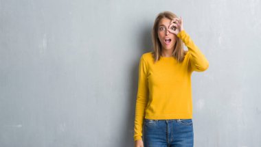 Sürpriz yüz, göz parmaklarının arasından seyir ile ok jest yapıyor grunge gri duvar üzerinde duran güzel genç kadın şok. İmansız ifade.