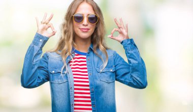 Güzel sarışın genç kadın giyiyor güneş gözlüğü izole arka plan üzerinde dinlenmek ve gülümseyen gözlerle kapalı parmak jestle meditasyon yapıyor. Yoga kavramı.