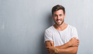 Üzerinde gri grunge Duvar ile mutlu yüz gülümseyen yakışıklı genç adam kameraya seyir silah geçti. Olumlu bir kişi.