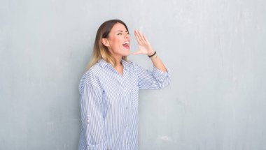 Genç Yetişkin kadın moda iş kıyafeti bağırarak ve ağzı üzerinde el ile yan için çığlık gri grunge duvarın üzerinden. İletişim kavramı.