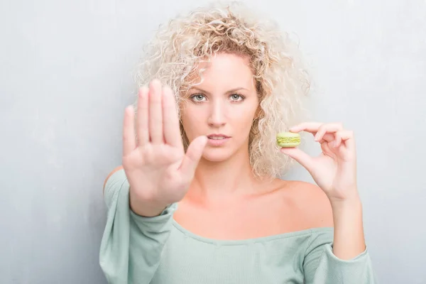 Joven Rubia Sobre Fondo Gris Grunge Comiendo Macaron Con Mano —  Fotos de Stock