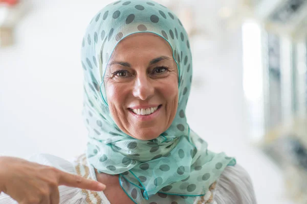Middle age brunette arabian woman wearing colorful hijab with surprise face pointing finger to himself