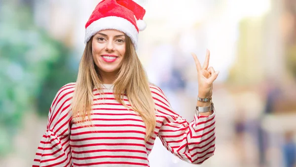年轻美丽的妇女戴着圣诞节帽子在孤立的背景微笑与快乐的脸眨眼在相机做胜利标志 第二个 — 图库照片