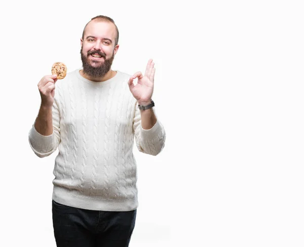 流行に敏感な若い男 優秀なシンボルの指で サインを行う分離の背景にチョコチップ クッキーを食べる — ストック写真